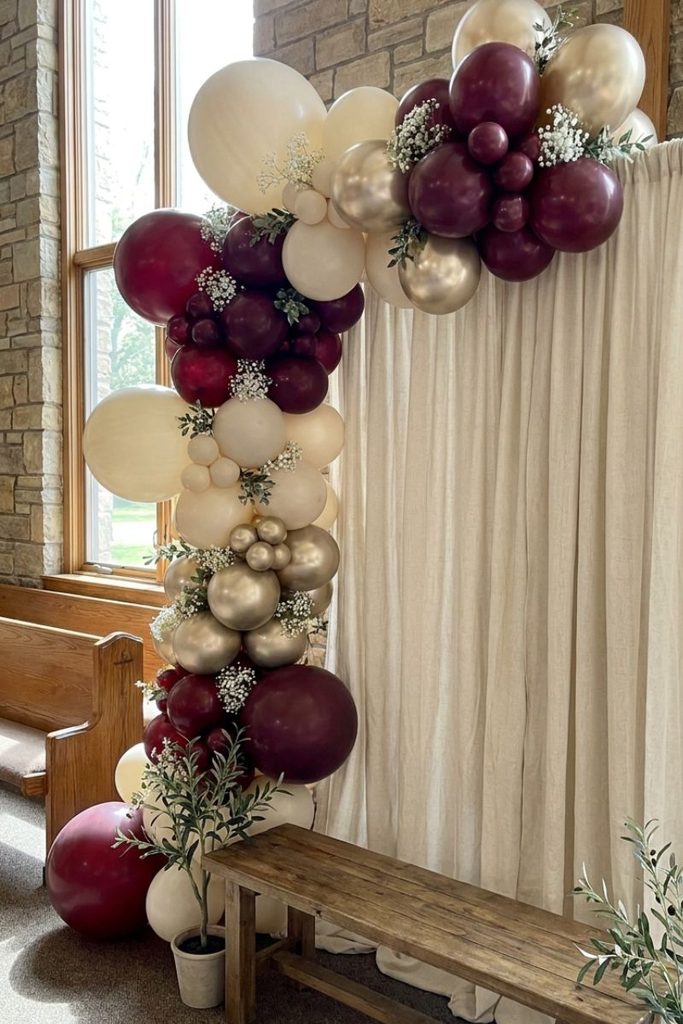 Pastor day decorations ideas with a burgundy, ivory, and champagne gold balloon arch.