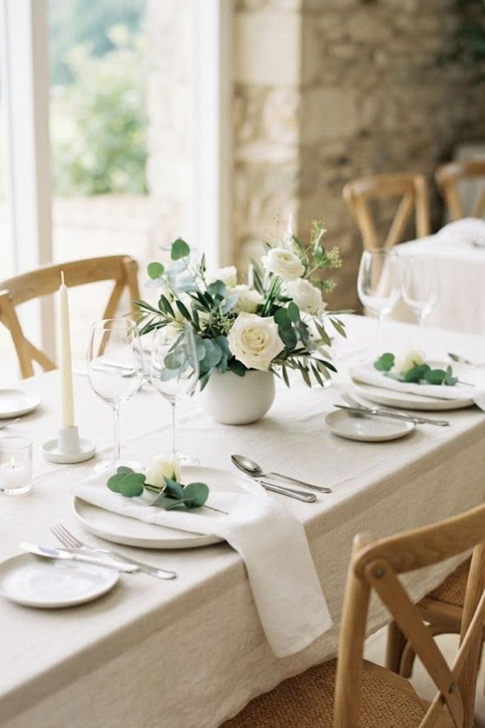Minimal wedding table decor with white flowers, ivory linen, clear glassware, and eucalyptus